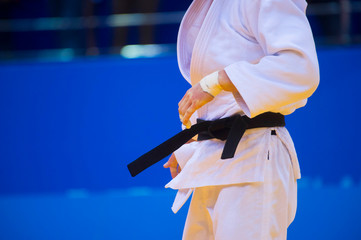 Judo fighter poses in white kimono with black belt. Japanese judo and jiu jitsu