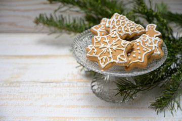 Gingerbread cookies for Christmas on a crystal glass bowl and decoration from fir branches on a white painted wooden table, copy space