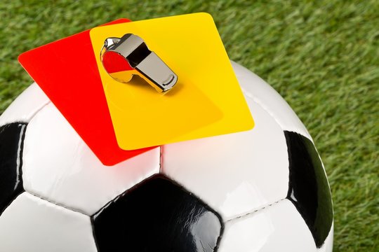 Close up of referee yellow and red cards and chrome whistle on top of soccer ball over grass background - penalty, foul or sports concept