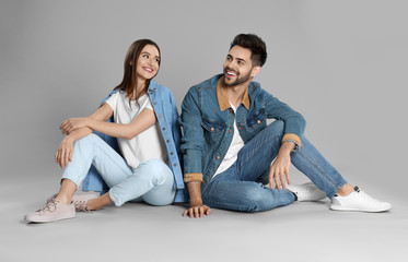 Young couple in stylish jeans sitting on grey background