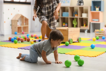 Fototapeta premium Young nanny and cute little baby playing with toys at home