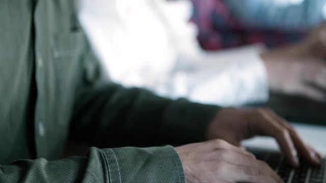Side view of focused developer in eyeglasses working with laptop. Young people sitting in row and typing on laptops. Technology concept