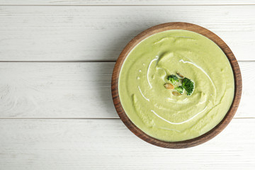 Delicious broccoli cream soup served on white wooden table, top view. Space for text