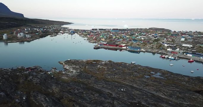 4K Aerial Drone flight in Disko Bay Greenland. Arctic city of Qeqertarsuaq in Disko Island. Colourful houses during sunset and midnight sun. Icebergs in Background.