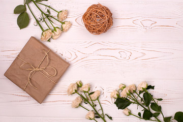 Gift box wrapped in kraft paper, rattan balls and flower on a white wooden background from above. Flat lay.