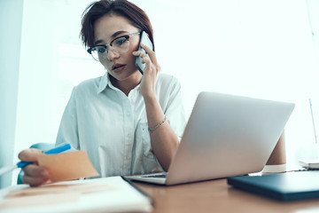 Young lady is talking on smartphone at workplace