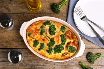 Tasty broccoli casserole in baking dish on wooden table, flat lay