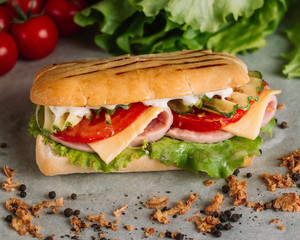 Preparing a crusty fresh ciabatta baguette sandwich in the kitchen with fresh salad ham serrano cherry tomatoes, olive oil and mozzarella cheese. Superfood sandwich on wooden rustic background