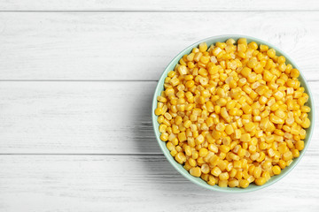 Delicious canned corn in bowl on white wooden table, top view. Space for text