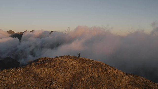 Flying around a hiker at the summit of a mountain. Sunset scene. 