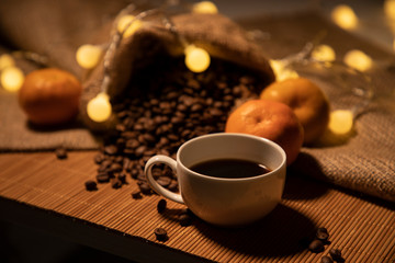 Magical still life with a cup of brewed coffee, coffee grains and tangerines. Comfort and tranquility. Horizontal photo