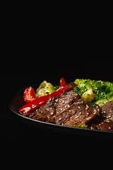 Beef Steak Salad. Close Up of a fresh green vegetables and bell pepper with sliced beef tenderloin steak. Black background Copy-paste space