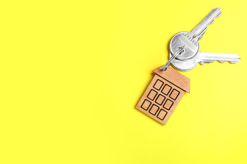 Keys with trinket in shape of house on yellow background, top view and space for text. Real estate...