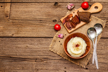 Homemade Thanksgiving garlic mashed potatoes with fresh tomatoes and pastrami. Sackcloth napkin, spoons, old wooden boards background