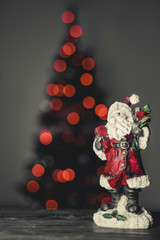 Close up image of a ceramic Santa Claus figure. Out of focus christmas three in the background. Bokeh of christmas lights.
