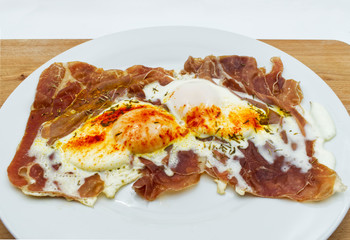  Fried eggs with ham in a white dish on wooden table