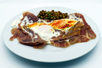 Fried eggs with ham and green peas in a white dish, isolated on white