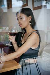 Asian girl in a cafe. Beautiful Balinese women with glass of wine with window reflection