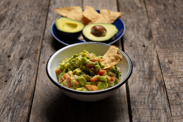 Mexican guacamole with tomato on wooden background
