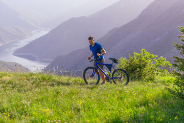 Tired fit mountain biker pushing his bike uphill at the top of the mountain on a sunny day with...
