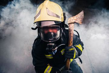 Obraz premium Portrait of a female firefighter while holding an axe and wearing an oxygen mask indoors surrounded by smoke.