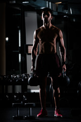 Fototapeta na wymiar Slim muscular man lifting weights in the gym