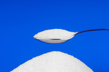 Spoon with white sugar on a blue background