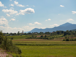 Fototapeta na wymiar Paisajes de campo y naturaleza rurales con un campanario nubes y montañas al fondo en la zona de Lipovac , Croacia, verano de 2019