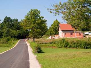 Fototapeta na wymiar Paisajes de campo y naturaleza rurales con una carretera pasando por delante de una casa con árboles en la zona de Lipovac , Croacia, verano de 2019