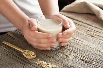 Oat milk in the glass on the wooden background.
