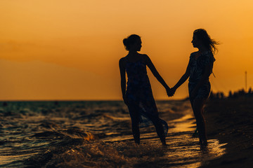 Relax girls in summer dress standing on beach sunset