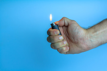 Hand with a gas lighter on a blue background. Hand with a lit gas lighter, portable device used to create a flame. Hand holds a burning gas lighter