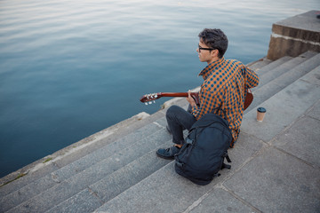 Young guy sitting on steps while playing guitar