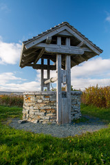A wishing well or water well with a wood roof and a rock base. The well is on gravel with green...