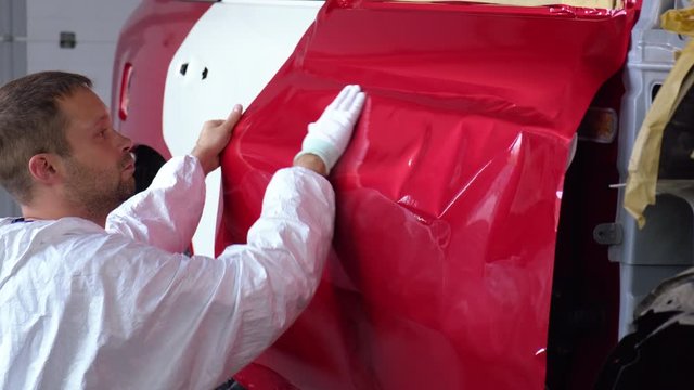 worker man is covering doors of automobile by tape, during repair works