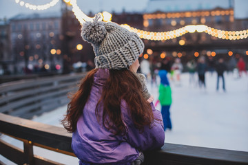 Girl watching on the ice rink with happy people ice skating in the background, concept of ice...