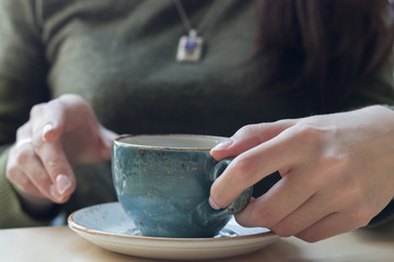 Fototapeta na wymiar Girl in a green sweater holding a blue cup of coffee on a saucer