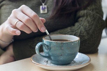 Horizontal photo with a girl who stirs a spoon of coffee in a blue cup on a saucer