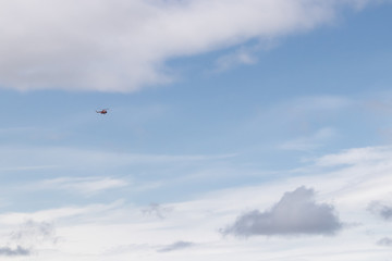 Fototapeta premium A helicopter flies through the blue sky among white clouds