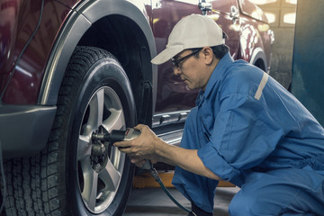 Asian male mechanic, carrying electric drill remove the tire changing car in garage Repair service.