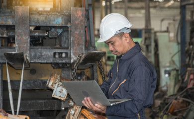Engineers wear safety helmets, hold computers to control production, stand in front of forklifts in factories.