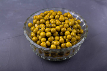 Canned green peas in a glass bowl on a gray background