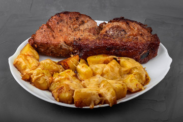 Pork loin steak and potatoes baked with cheese on a white plate