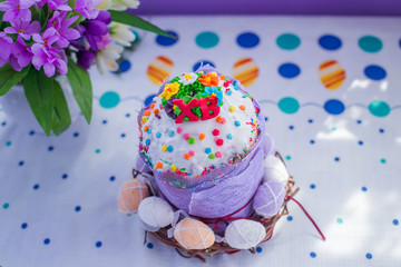 homemade cake decorated with multicolored sweets and ukrainian letters XB . Painted eggs in basket around cake for Easter on table with beautiful Easter table.