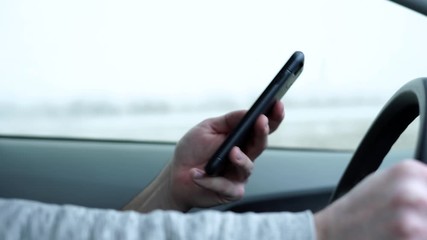 Man with cell phone texting while driving in snowy wet conditions on the highway being irresponsible, dangerous, selfish, lazy, and reckless