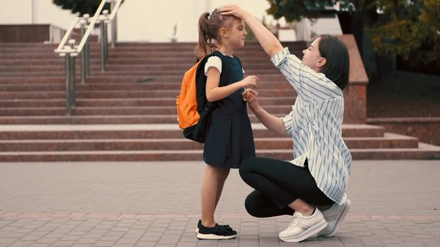 A European mother is preparing her daughter for school classes. The student and mother are standing at an educational establishment. The pupil is wearing the school uniform.