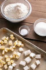 Top down view on a sheet tray of butter, beside bowls of baking ingredients