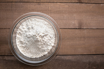 Flat lay of baking flour in a glass bowl, on a wood counter with space for text