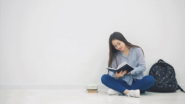 Young asian girl involved in the process of reading book while sitting on the floor in lotos position.