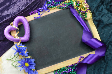 A blackboard surrounded by Mardi Gras decorations and purple and green fabric